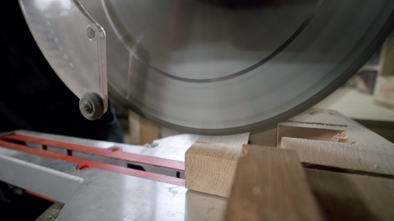 천천히 찍은 장면에서, 주인은 작은 가구 제조업체의 목재 작업실에서 원형 도자기로 나무판을 잘라낸다.