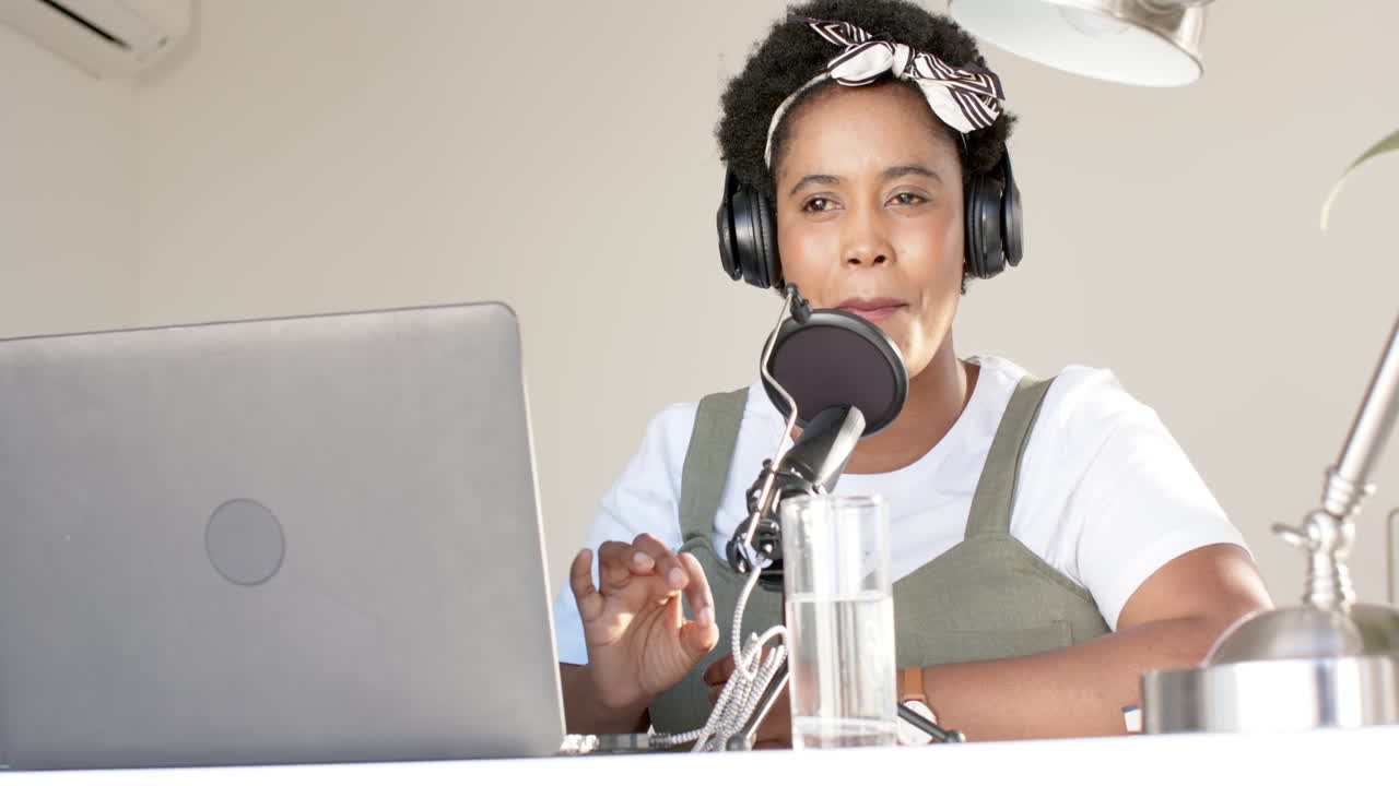 una mujer afroamericana graba un podcast en casa, con auriculares.
