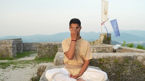 Slow-motion-of-Asian-Indian-man-doing-nadhi-shuddhi-meditation-at-sunrise-on-stone-wall-on-top-of-the-hill