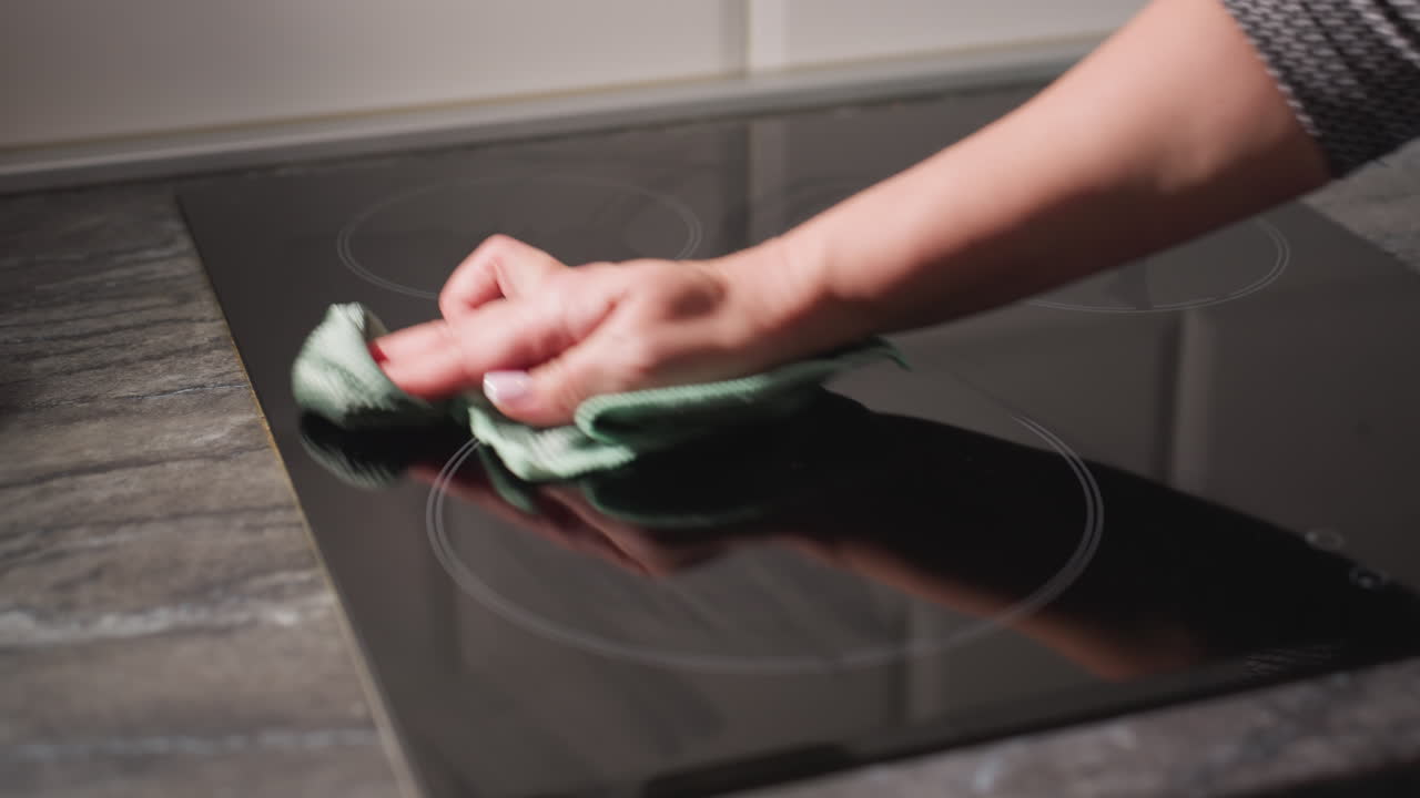 Close up hand cleaning electric stove glass surface with green cloth in modern kitchen showing hygiene care responsibility reflection on smooth surface
