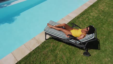 Mujer-De-Raza-Mixta-Sentada-En-Una-Tumbona-Tomando-El-Sol-Junto-A-La-Piscina