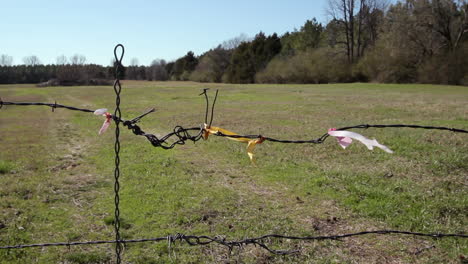 flagging tape tied to a section of barbed wire fencing in front of a grassy pasture on a windy day