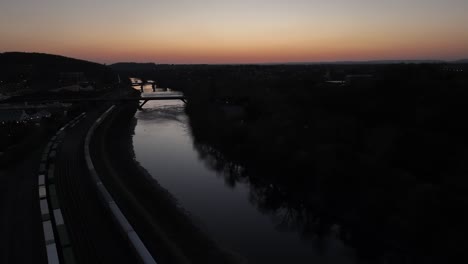 An-aerial-view-of-the-Lehigh-River-in-Bethlehem,-Pennsylvania,-after-sunset-with-long-cargo-trains-on-the-left-of-the-shot