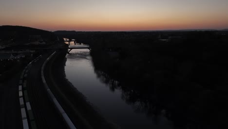 an aerial view of the lehigh river in bethlehem, pennsylvania, after sunset with long cargo trains on the left of the shot