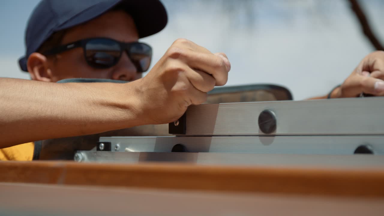 Close-up shot of a tourist un-pinning the rooftop ladder of his off-road vehicle as he starts to push the ladder out.