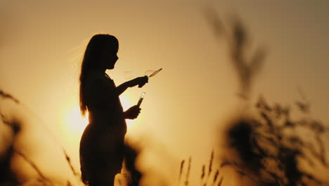 silhouette of a girl playing with soap bubbles in the tall grass at sunset