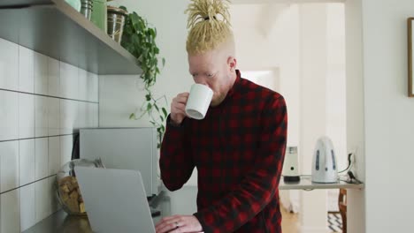 Thoughtful-albino-african-american-man-with-dreadlocks-using-laptop-and-drinking-coffee