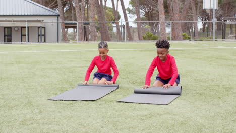 multiracial boys rolling yoga mats on school field, preparing for outdoor activity