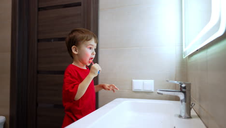 caucasian toddler in red t-shirt cleans teeth looking at the mirror. teeth hygiene of the child.