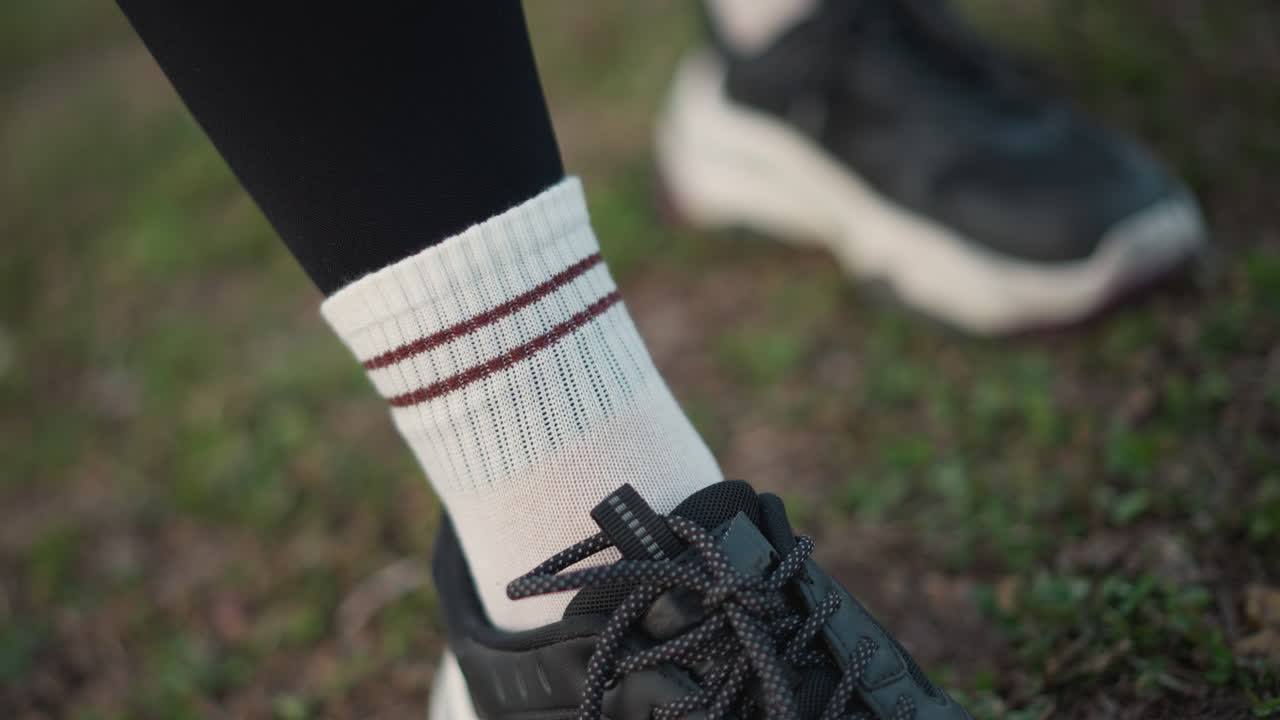 Athlete Adjusting Socks Before Run, Trail Runner Preparing For Morning Jog On Grass, Individual Tightening Sock Strap Above Sneaker As Part Of Running Gear Preparation In Natural Setting