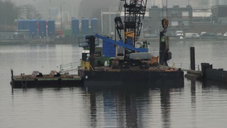 a crane and lift on a floating platform working on sheet pile installation in an industrial harbor