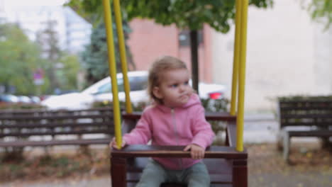 little girl with serious look on face being pushed on swing by her dad