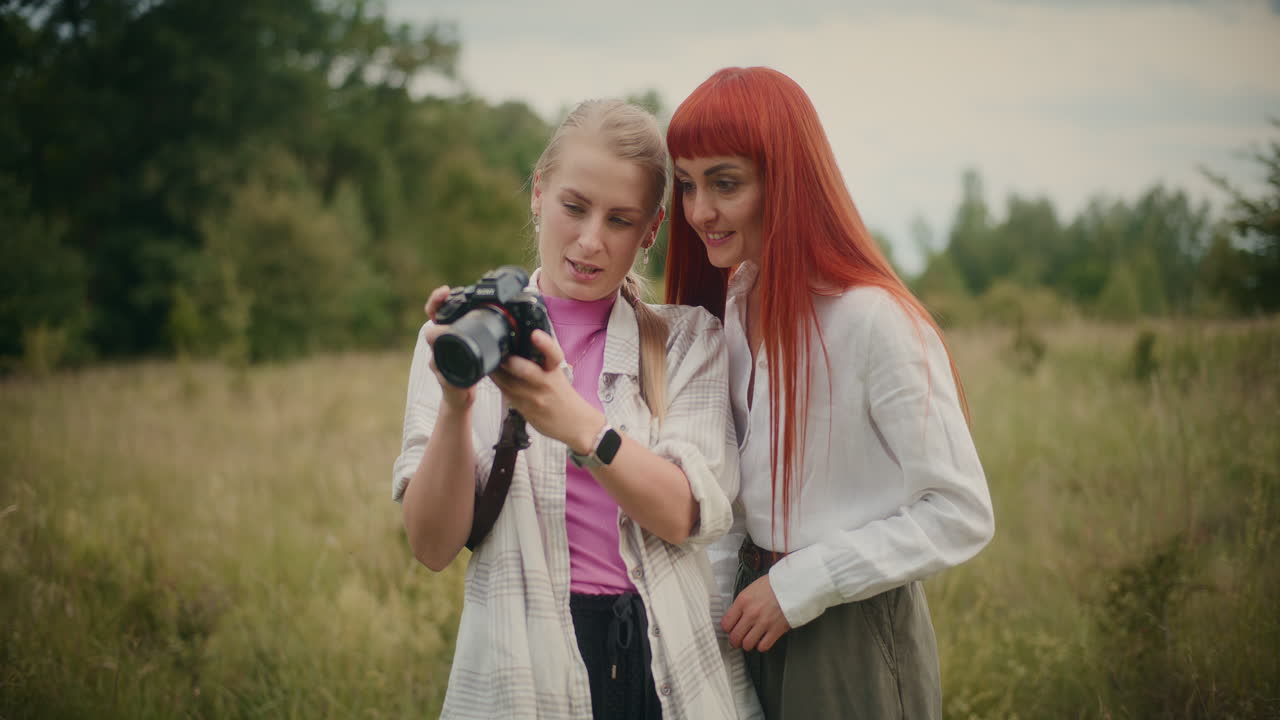 Two women looking at photos on a camera in a field