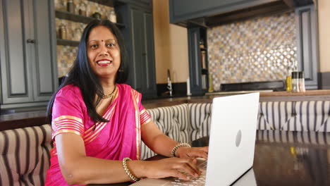 working from home, indian woman in traditional sari using laptop in modern kitchen