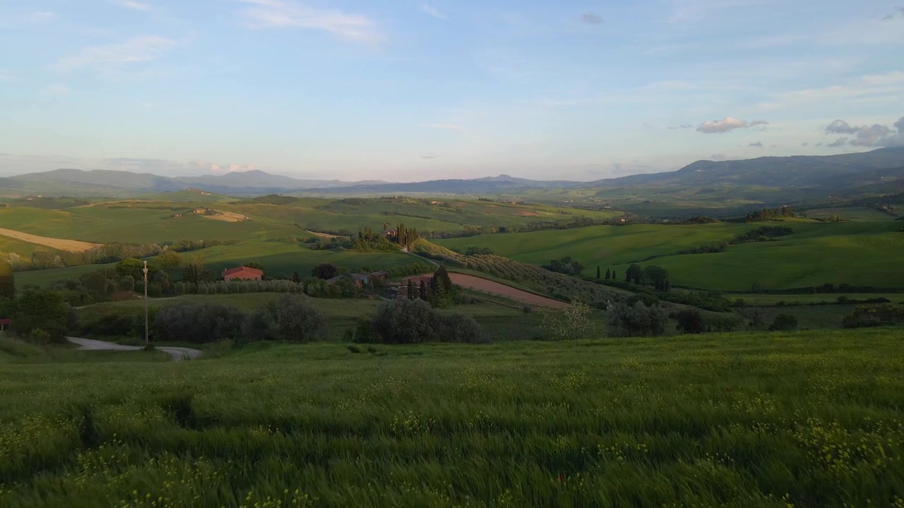 Una mozzafiato ripresa aerea cinematografica della lussureggiante campagna toscana con dolci colline, ville tradizionali e un sereno tramonto estivo. Ideale per contenuti di viaggio e benessere