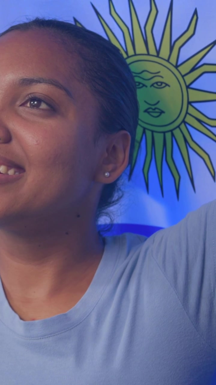 Vertical video: Raising woman in blue tee lifting right arm and posing by sun graphic in room