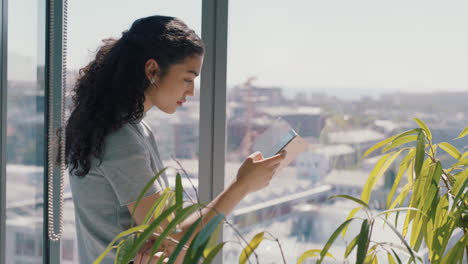 beautiful business woman using smartphone texting female executive checking emails browsing messages on mobile phone in office standing by window with view of city