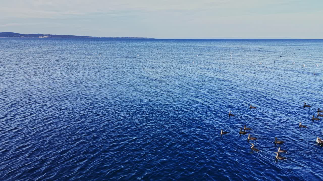 Vast blue water stretches across a calm sea with distant land visible