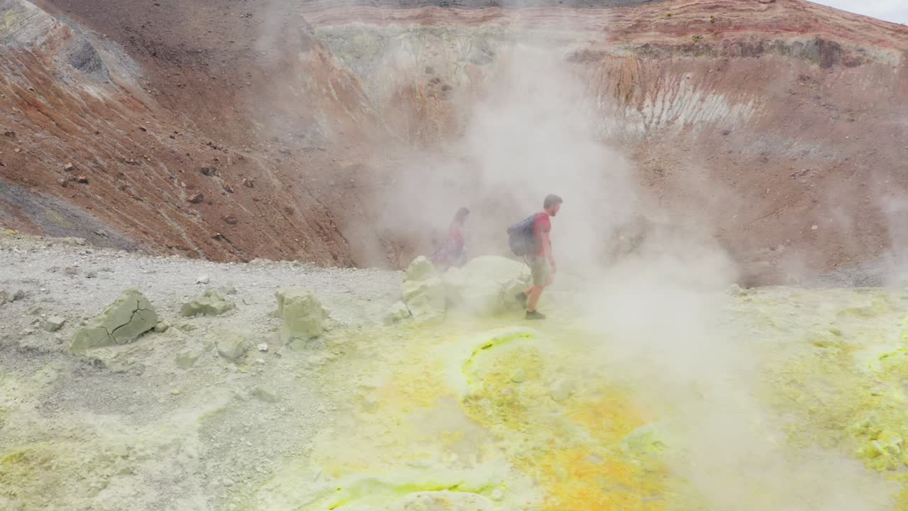 vista panorámica de una pareja caminando a través de los humos sulfurosos del volcán, inclina la cámara hacia el cráter