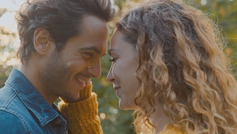 un primer plano de una feliz pareja enamorada sonriendo mientras el hombre levanta a la mujer mientras se abrazan juntos en el parque de otoño.