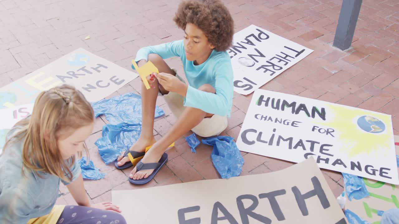 Video de un niño y una niña de diversas etnias haciendo carteles de protesta en el patio de la escuela, espacio para texto