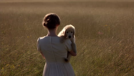 woman carrying a puppy through a sunlit field
