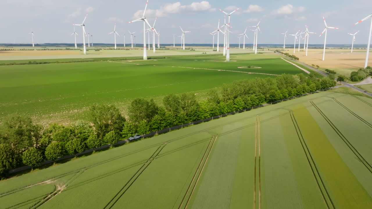 Aerial view tilting toward a RV driving close to wind turbines, summer day