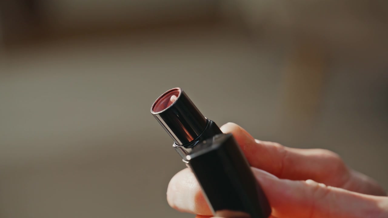Woman hands holding lipstick taking off cap twisting cosmetic tube closeup.