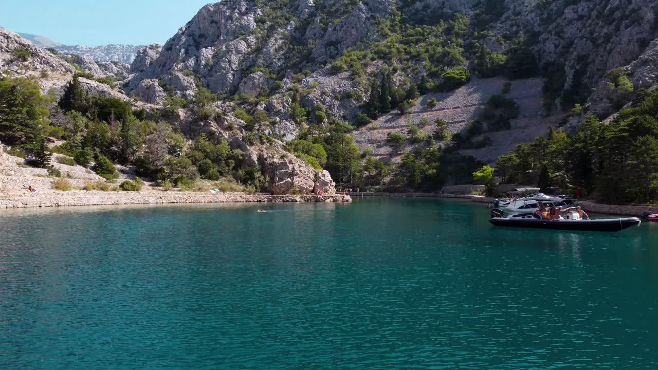 Aerial forward flight over clear water of Zavratnica Bay with resting people ion boat and swimming person in summer