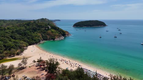 drone footage captures nai harn beach in phuket, thailand, showcasing turquoise waters, sandy shores, and anchored boats under clear skies