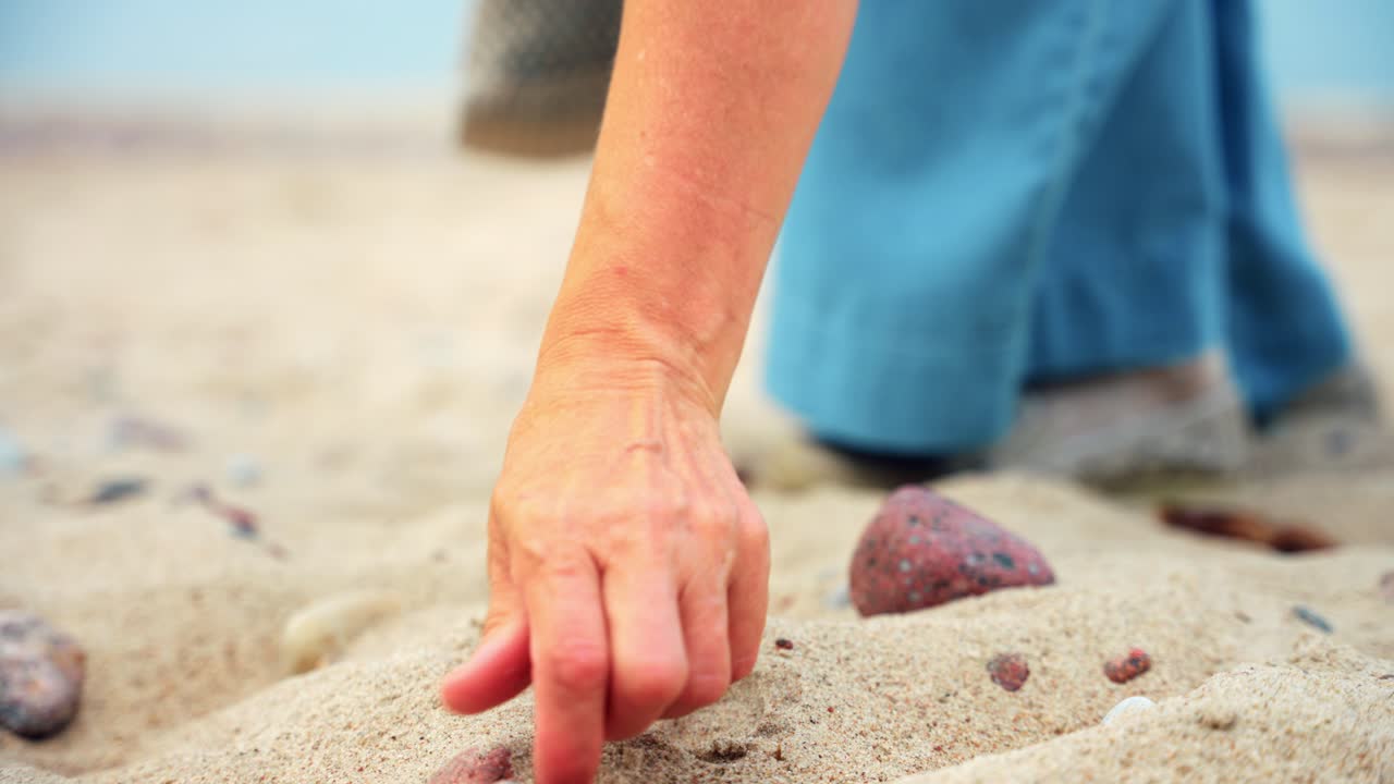 mujer adulta media recogiendo piedras en el paseo marítimo de arena en la playa de karkle, lituania