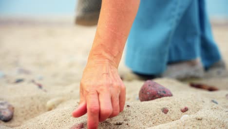 Mujer-Adulta-Media-Recogiendo-Piedras-En-El-Paseo-Marítimo-De-Arena-En-La-Playa-De-Karkle,-Lituania