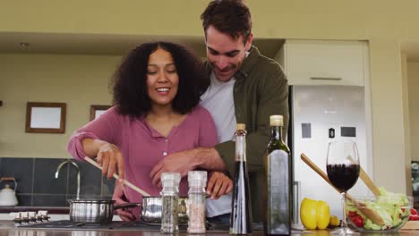 happy diverse couple preparing a meal together in kitchen, smelling food and embracing