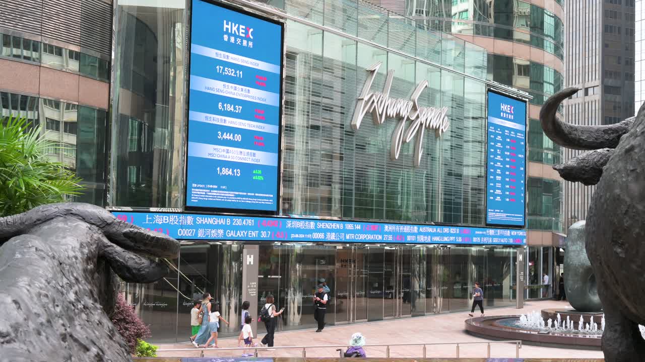 People walk past a moving screen displaying negative stock ticker symbols at Exchange Square, home to the Hong Kong Stock Exchange (HKEX), in Hong Kong's financial district.