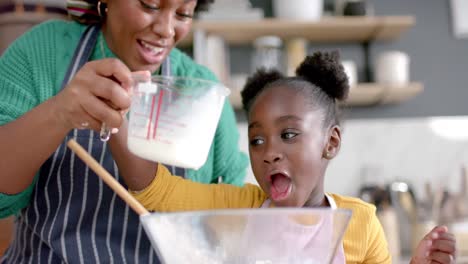 happy african american mother and daughter preparing dough in bowl in kitchen, slow motion