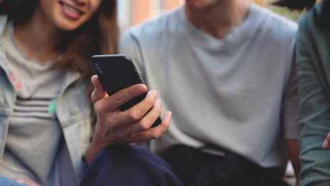 close up of three young japanese friends looking something on mobile phone while sitting together in the park