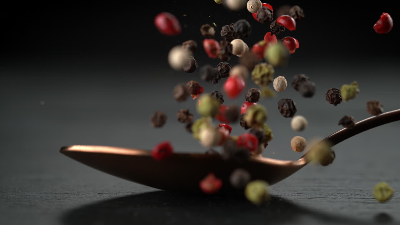 Spoon Of Pepper Blend Falls Onto The Stone Kitchen Board And The Spice Scatters in Macro and Slow Motion
