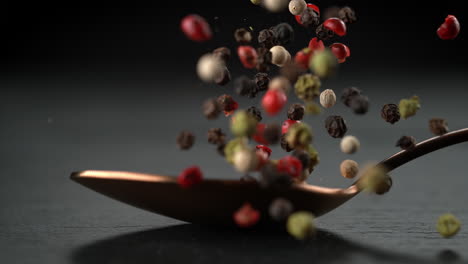 ein löffel pfeffermischung fällt auf die steinerne küchenplatte und das gewürz verstreut sich in makro- und slowmotion