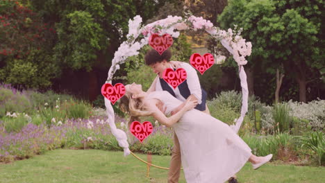 Animación-De-Corazones-Rojos-Te-Amo-Sobre-Una-Feliz-Pareja-Diversa-Abrazándose-En-El-Jardín-El-Día-De-La-Boda