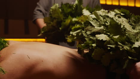 man receiving a sauna treatment with herbal branches