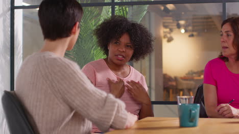 woman wearing pink breast cancer awareness ribbon talking at meeting of therapy support group for cancer treatment patients 1