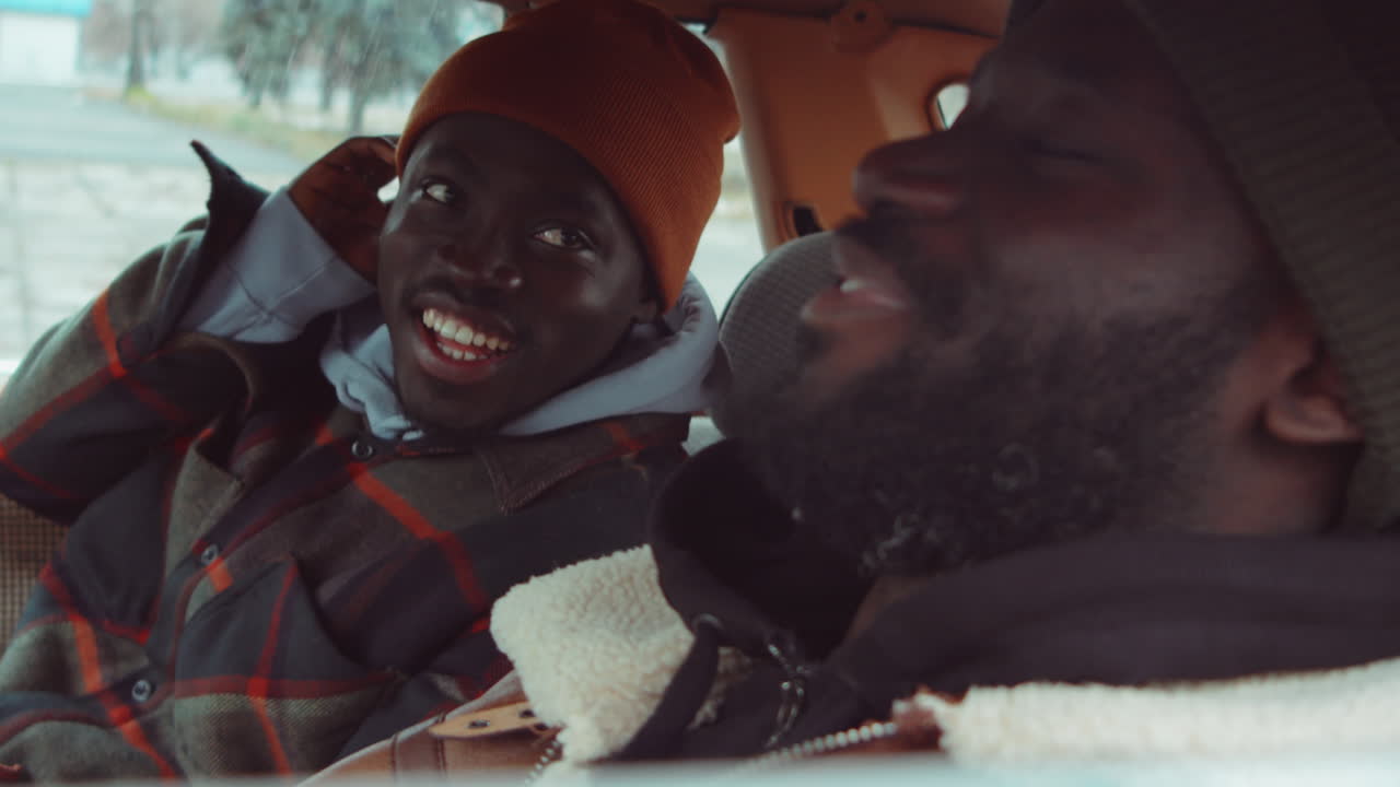 두 명의 아프리카계 미국인 남자들이 차에서 미소 짓고 대화하고 있습니다.