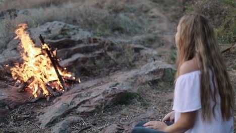 young woman sitting near campfire. young girl sitting near campfire in nature at evening