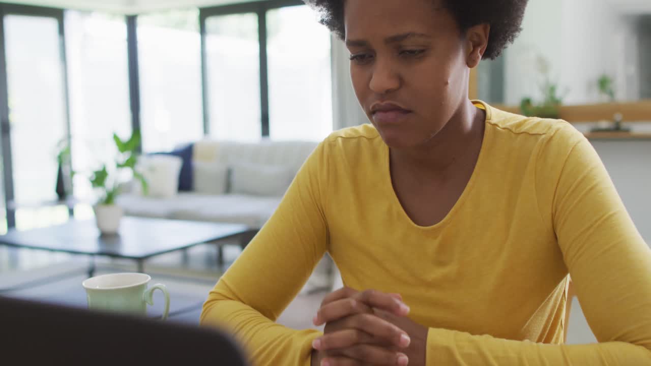 Tired african american woman sitting at table using laptop