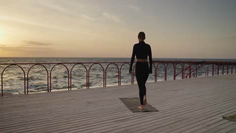 woman practicing yoga at sunset on a wooden dock by the sea
