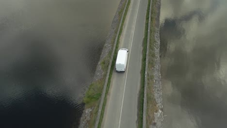 Furgoneta-De-Reparto-A-Lo-Largo-De-La-Carretera-Estrecha-Sobre-El-Embalse-De-Vartry-En-Madera-Redonda-Con-Nubes-Reflejo-En-El-Agua-En-El-Condado-De-Wicklow,-Irlanda