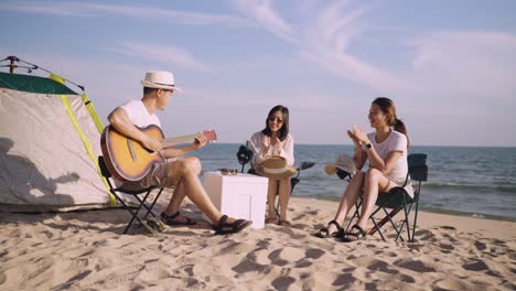 행복한 아시아 친구 그룹은 야외 휴가 여름에 해변에서 피크닉과 캠핑을 할 때 기타를 연주하고 박수를 치며 노래합니다.