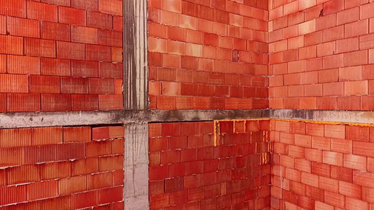 Factual close up of hollow clay blocks layered with mortar within a concrete structural column framework. Interior corner view of red ceramic brick walls. Aerial view.