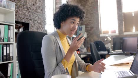 feliz mujer de negocios casual biracial usando un teléfono inteligente en la oficina en cámara lenta