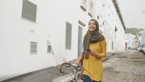 woman wearing hijab holding a bike behind her and using phone